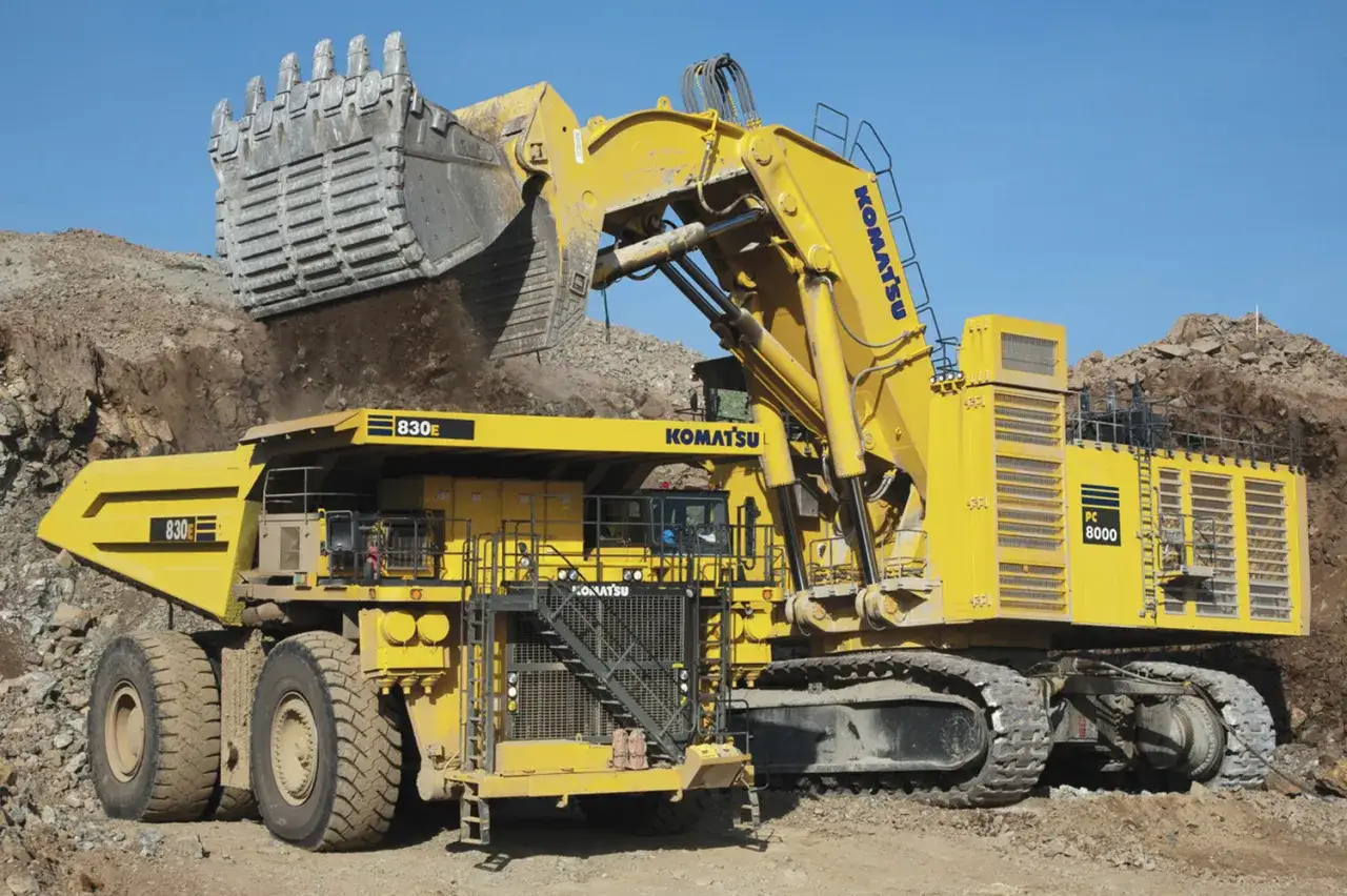 Największa koparka Komatsu PC 8000 z ogromną łyżką zasypuje ziemią potężną wywrotkę 830E.