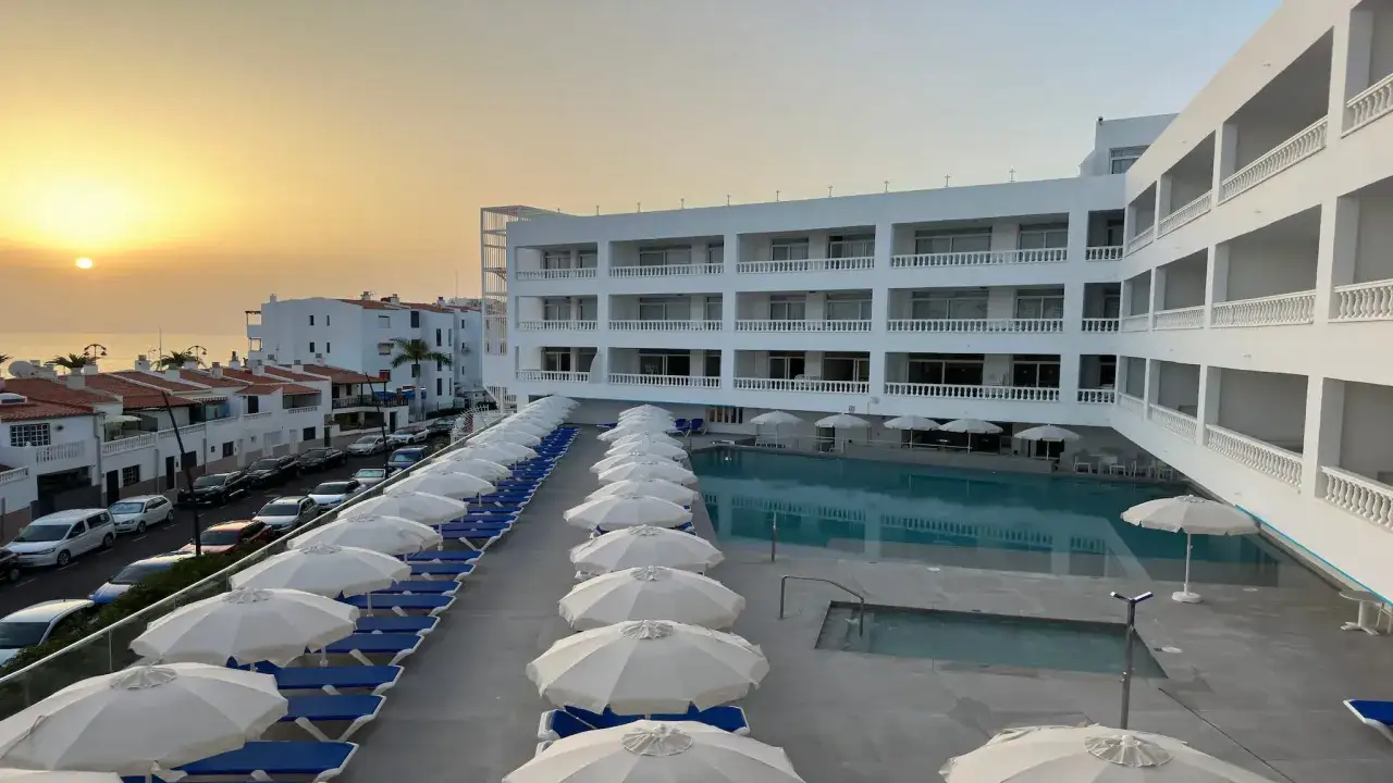 Atardecer sobre el mar azul, con un hotel moderno y una piscina. Un día perfecto en Lagos de César.