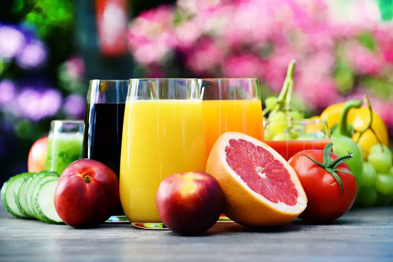 Vasos de zumos de naranja, uva y verde, junto a frutas y verduras. &iexcl;Cuidado! el zumo de naranja engorda si se abusa.