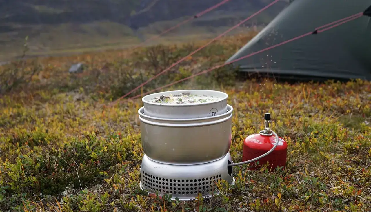 Matlagning i fjällen med en Optimus Svea. En kastrull med mat värms på en campingkök. Tält i bakgrunden.
