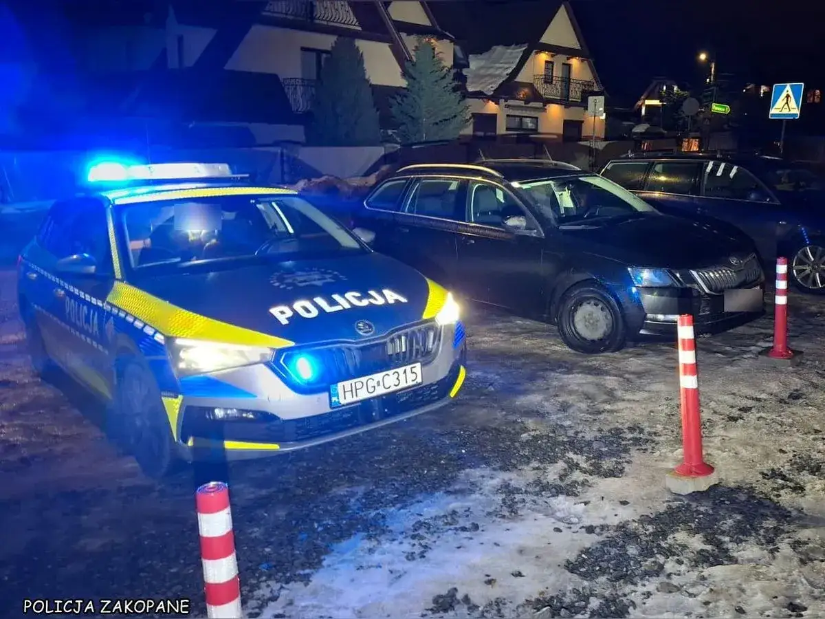 Radiowóz policyjny z włączonymi sygnałami świetlnymi przy dwóch samochodach. Prawdopodobnie kolizja w stanie nietrzeźwości.
