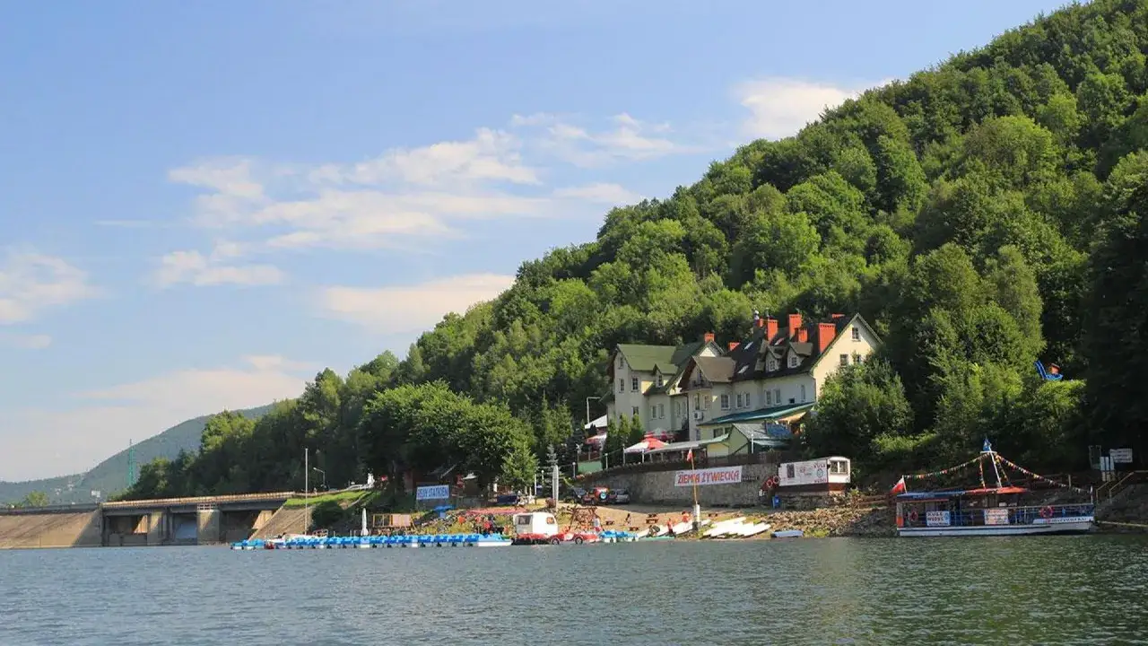 Malowniczy zbiornik wodny z zaporą, budynkami hotelowymi na zboczu i łodziami przy brzegu.
