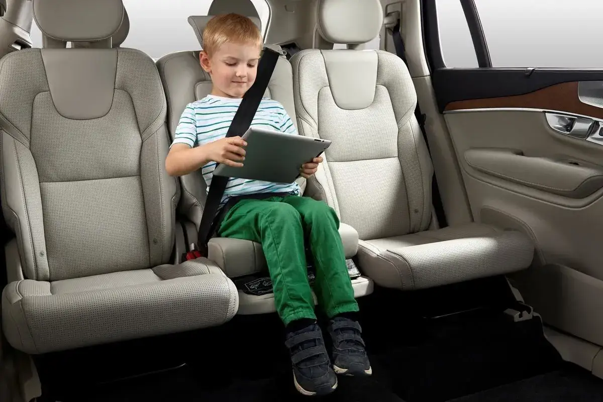 Niño con tablet, sentado en el coche sin silla, con cinturón de seguridad.