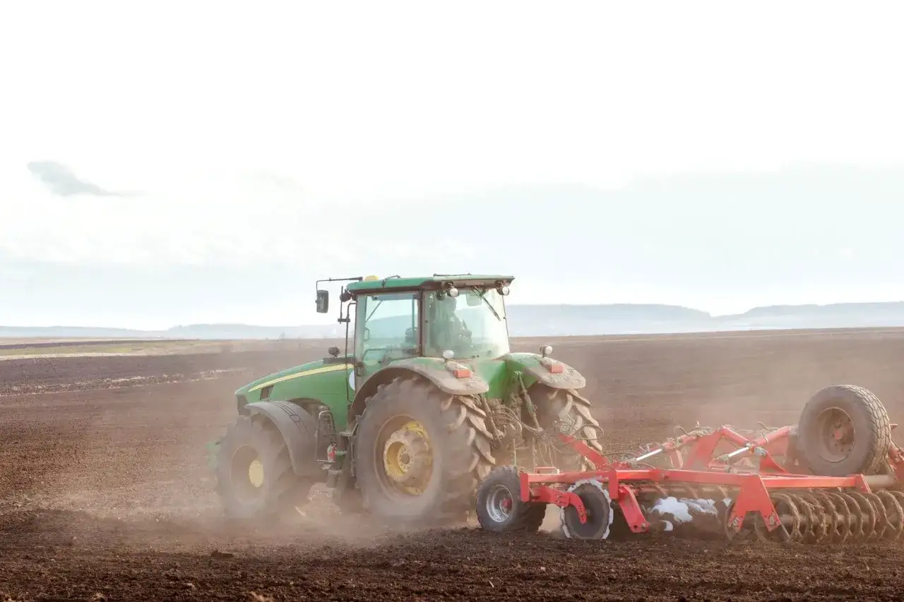 Zielony traktor z pługiem orze pole. Zastanawiasz się, ile kosztuje przepisanie gospodarstwa u notariusza?