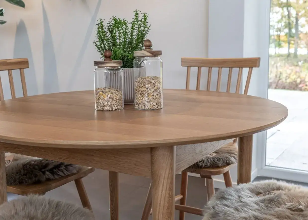 Runt matbord i trä med två glasburkar fyllda med müsli och en grön växt. Mysiga fårskinn på stolarna ger inspiration.