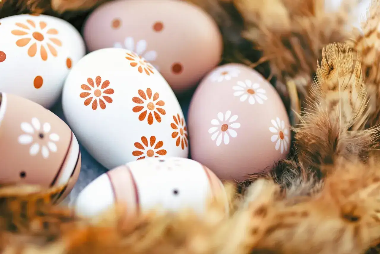 Ostereier mit Blumenmuster, einige braun, andere wei&szlig;, liegen in einem Nest aus Federn.