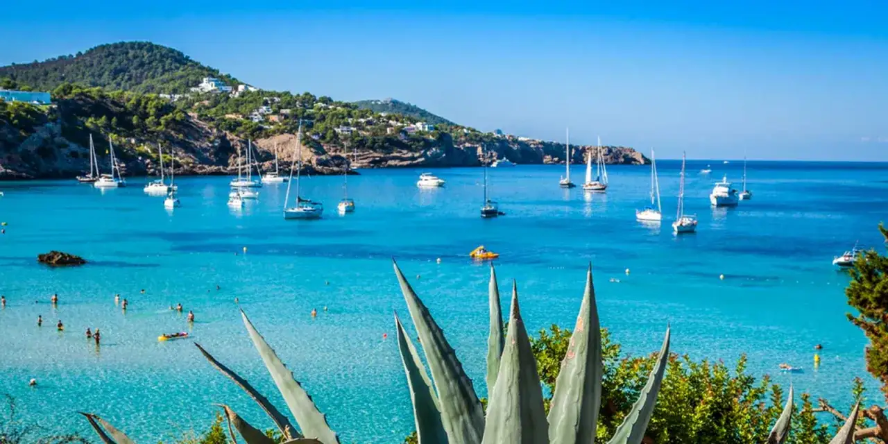 Vue idyllique d'une baie aux Bal&eacute;ares, avec des voiliers et des baigneurs. On imagine les &eacute;tudiants de l'universit&eacute; des &icirc;les bal&eacute;ares profiter de ce d&eacute;cor.