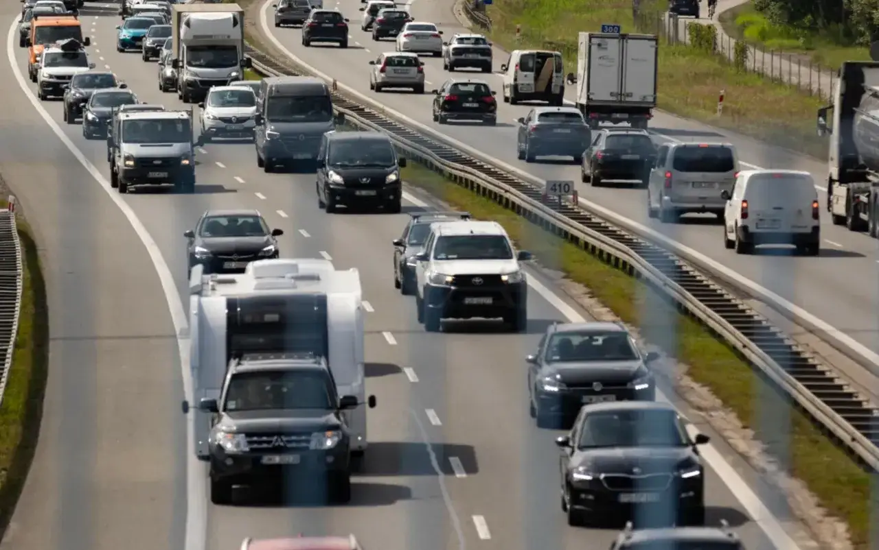 Samochód terenowy z przyczepą kempingową na autostradzie. Wiele pojazdów w ruchu, w tym ciężarówki i vany.