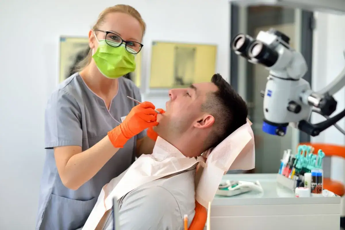 Dentystka w masce i rękawiczkach wykonuje zabieg. Pacjent siedzi na fotelu, czując znieczulenie u dentysty.