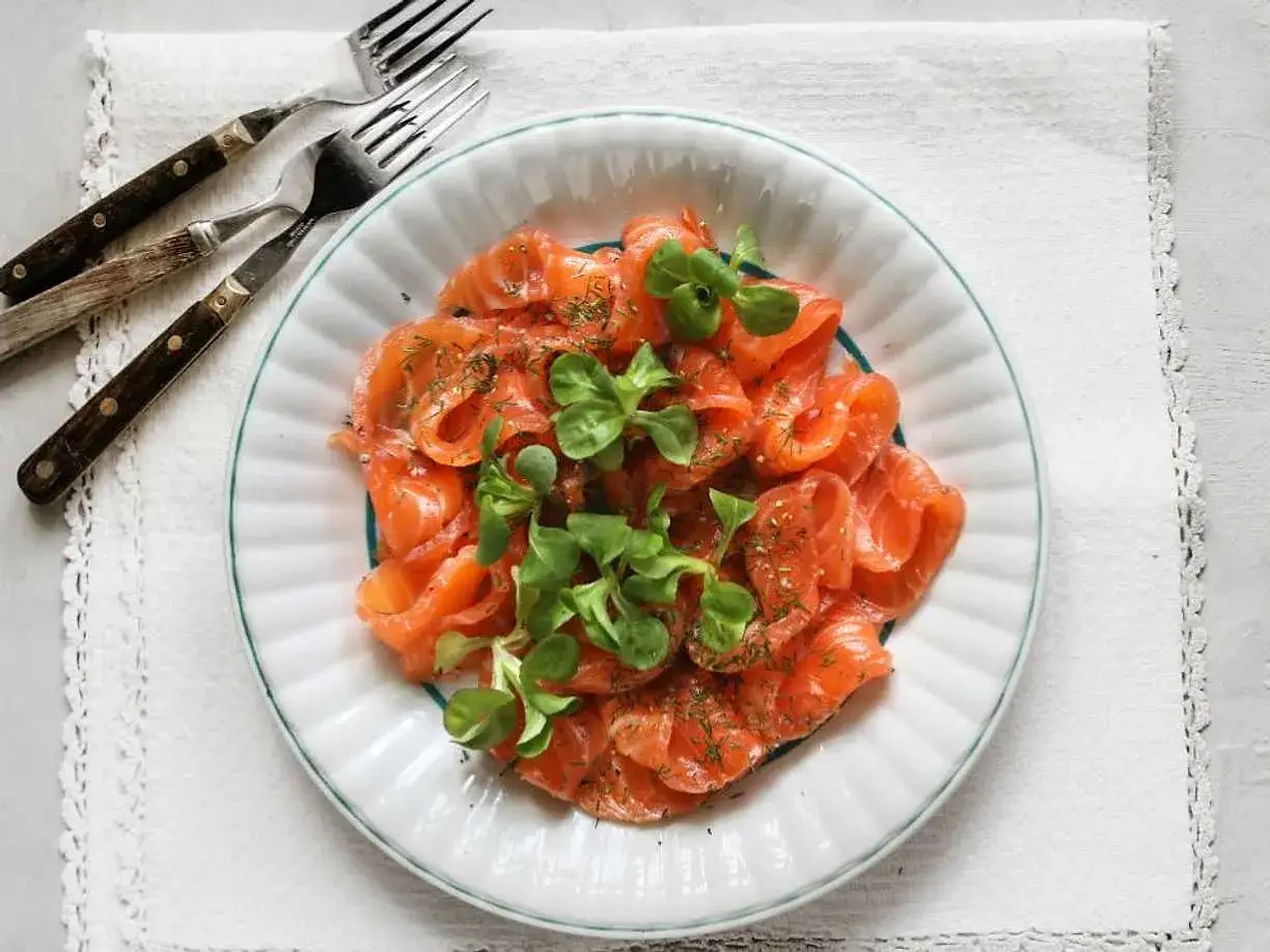 En tallrik med gravad lax, garnerad med dill och gröna blad. Frågan är om man kan frysa gravad lax för att spara den till senare.