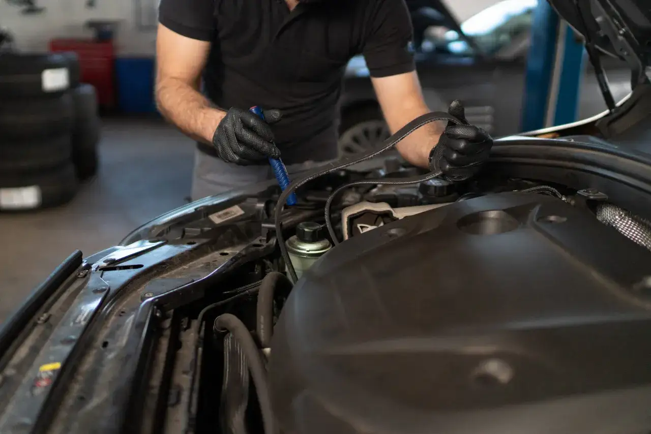Mechanik w czarnej rękawiczce trzyma pasek, przygotowując się do wymiany rozrządu w samochodzie.