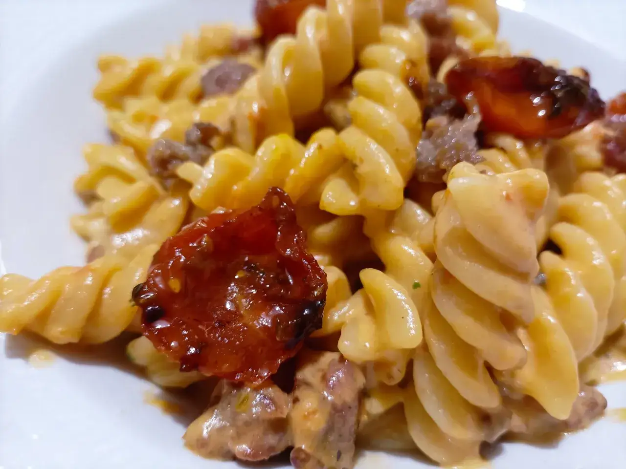 Fusilli cremosi con pezzetti di salsiccia e pomodorini confit. Un piatto invitante e saporito.