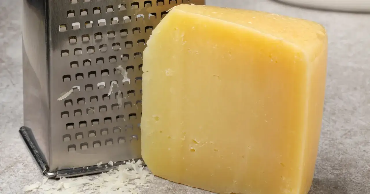 Kostka twardego, ż&oacute;łtego sera pecorino obok metalowej tarki. Widać starte kawałki sera.