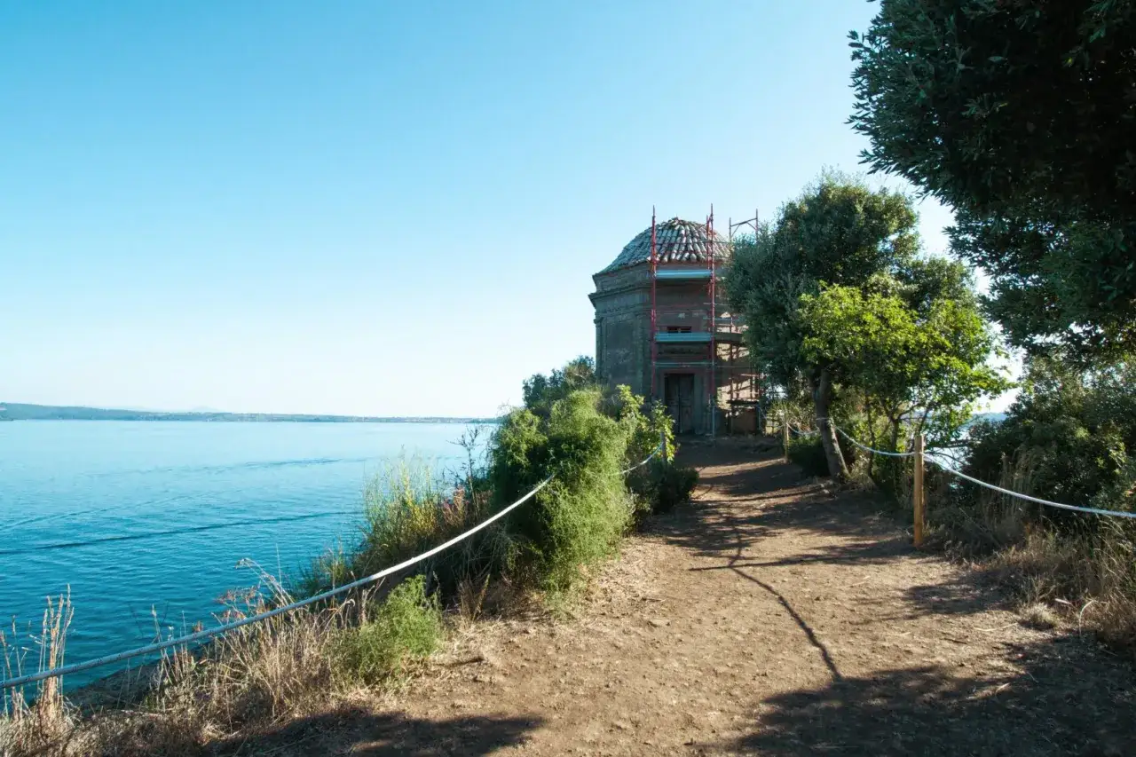 Sentiero sull'Isola Bisentina, con un edificio storico in restauro e il lago sullo sfondo. Una visita suggestiva.