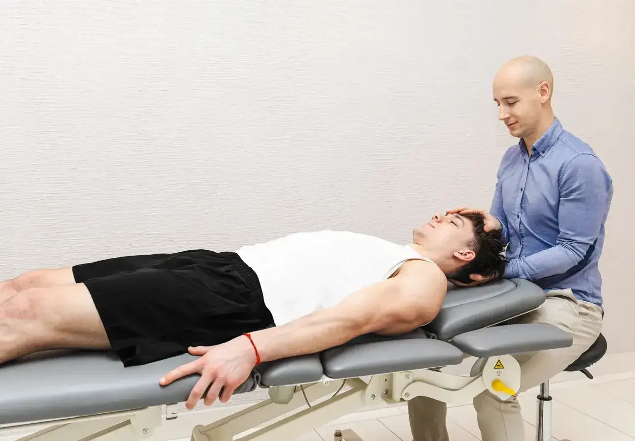 Osteopata wykonuje delikatny masaż głowy pacjenta leżącego na kozetce. Czy osteopata jest lekarzem? To pytanie często zadawane przez pacjentów.