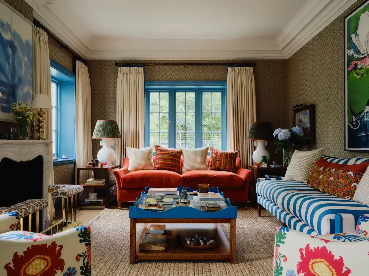 Salon confortable avec canapé orange, fauteuils fleuris et table basse bleue. La couleur encadrement fenêtre intérieur est d'un bleu vif, contrastant avec les rideaux crème.