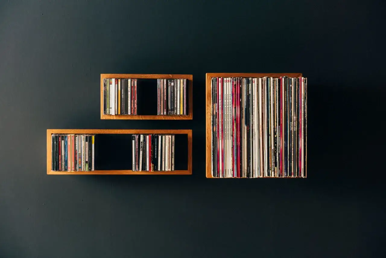 Drei Holzregale an einer dunklen Wand, gefüllt mit vielen bunten Schallplatten.