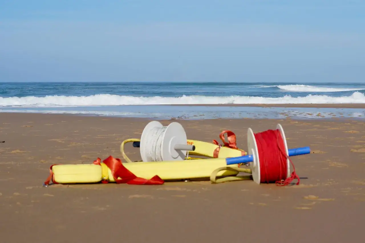 Sur la plage, un tube de sauvetage jaune avec des bobines de corde blanche et rouge, prêt pour une intervention.