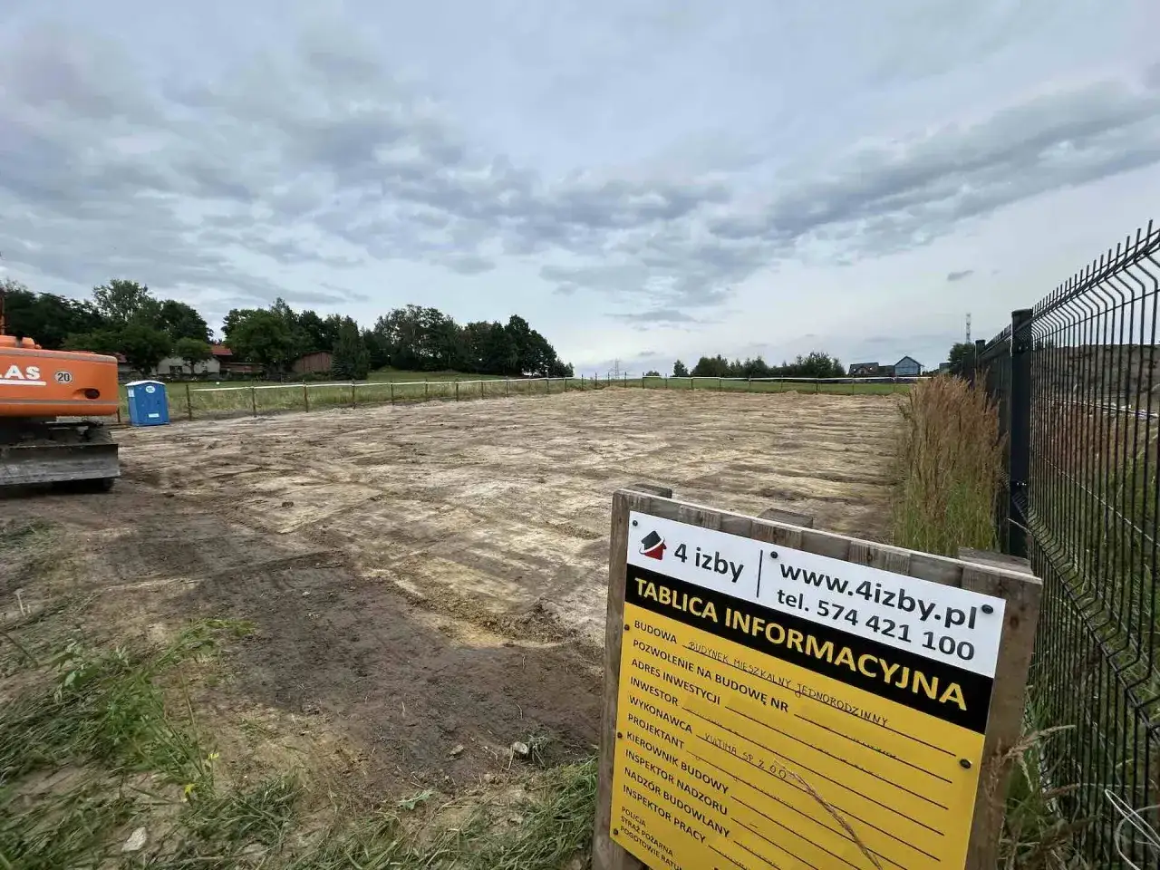 Tablica informacyjna budowy wyjaśnia, jak wypełnić dokumentację budowlaną. Plac budowy z koparką w tle.