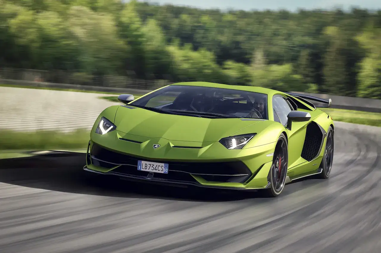 Un Lamborghini Aventador verde brillante acelera en una pista, con &aacute;rboles borrosos al fondo.