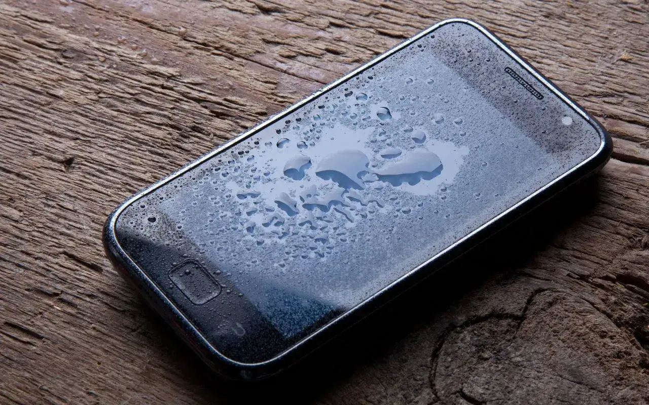 Zalany telefon na drewnianym blacie. Co zrobić jak telefon wpadnie do wody? Szybko wyłącz i osusz.