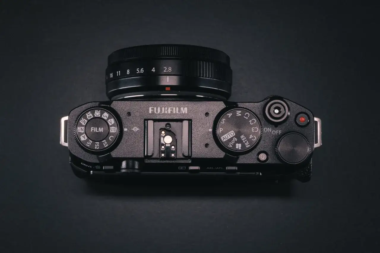 Vista superior de una c&aacute;mara Fujifilm X-M5 negra, con su lente y diales de control.