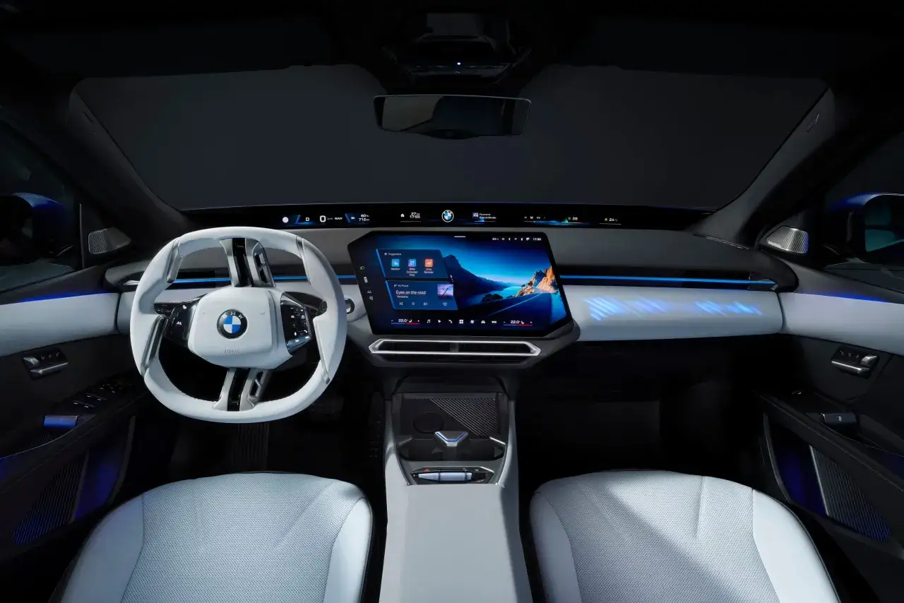 Wnętrze BMW i3 testowe: biała kierownica, duży ekran multimedialny z nawigacją, cyfrowe zegary i niebieskie podświetlenie.