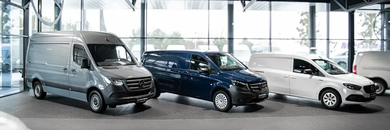 Trzy dostawcze samochody marki Mercedes-Benz: szary, granatowy i biały, stoją w salonie.