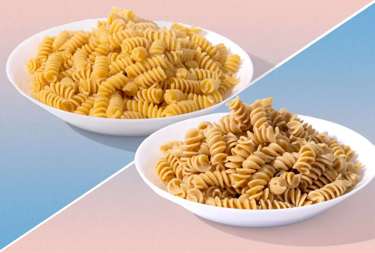 Dwa talerze makaronu fusilli: jeden jaśniejszy, zwykły, drugi ciemniejszy, proteinowy.