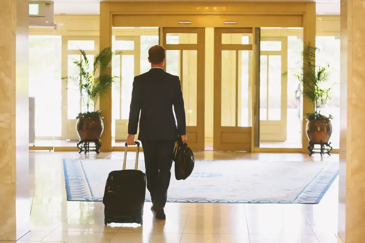 Mężczyzna w garniturze z walizką i torbą idzie przez hol hotelowy. Czy w hotelu obowiązuje cisza nocna?