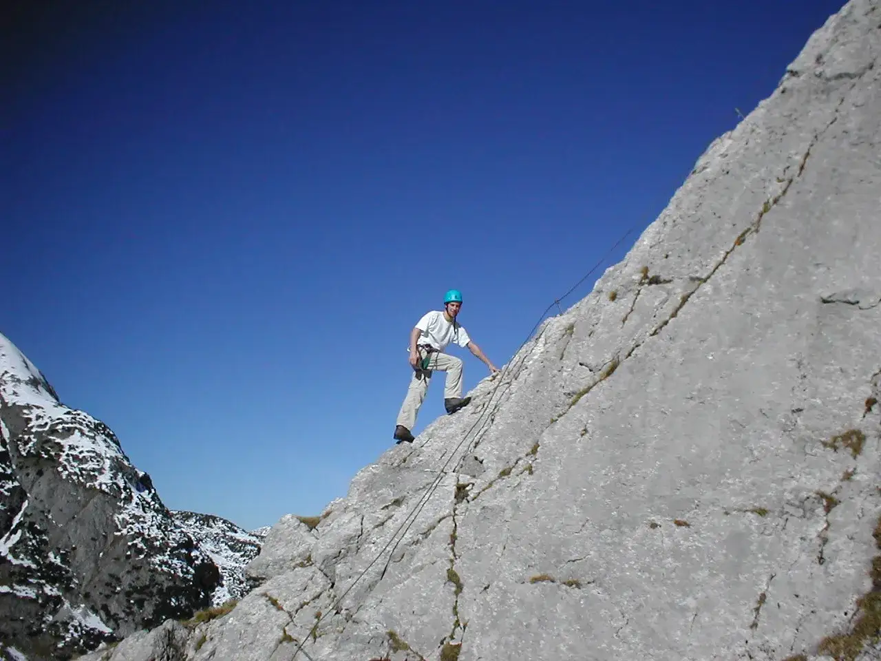 Ein Mann klettert gesichert am Seil den Tajakante Klettersteig entlang. Der blaue Himmel spannt sich &uuml;ber die felsige Berglandschaft.