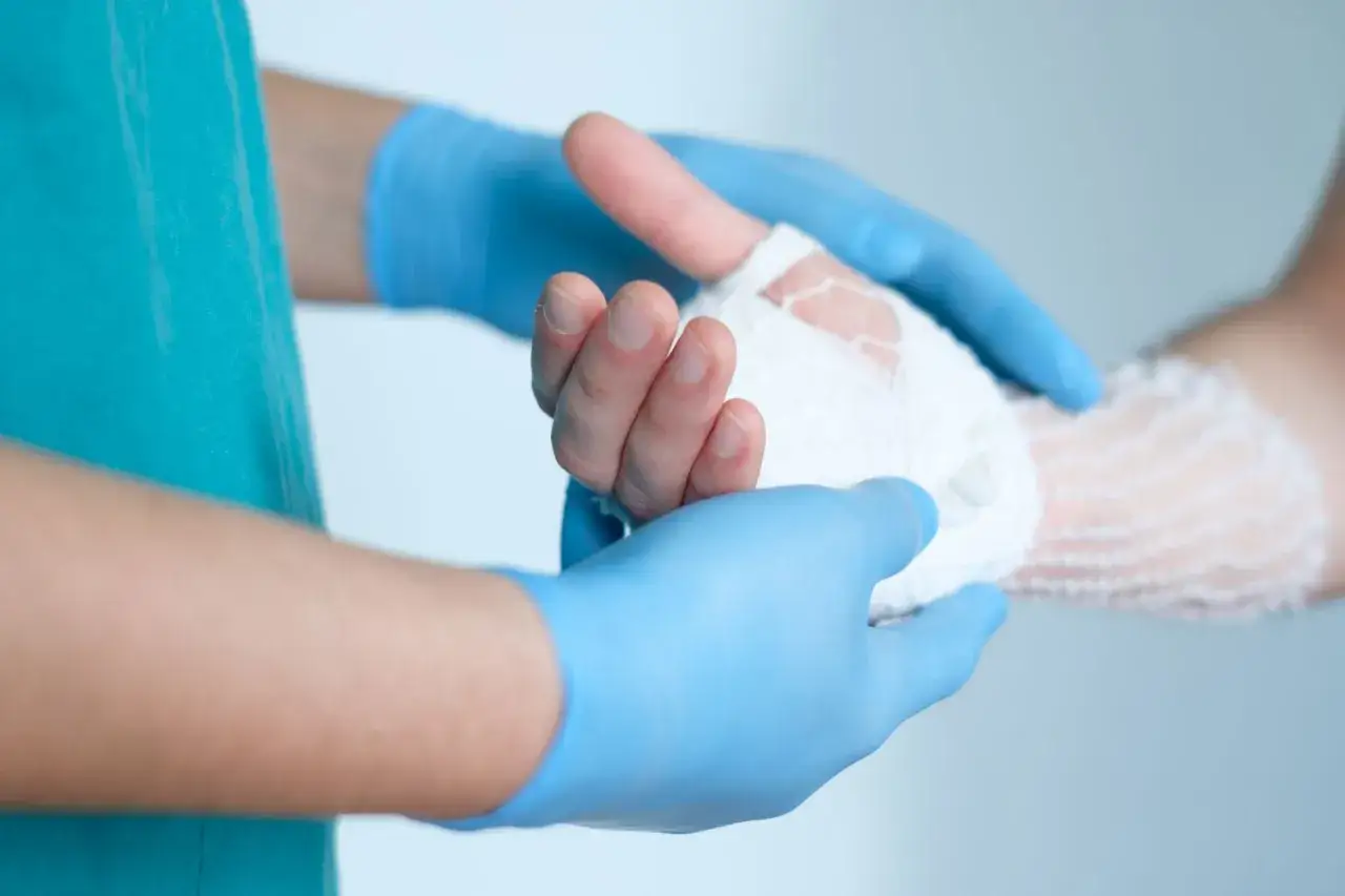 Sanit&auml;ter mit blauen Handschuhen wickelt einen Verband um eine Hand, um die Blutung zu stoppen.