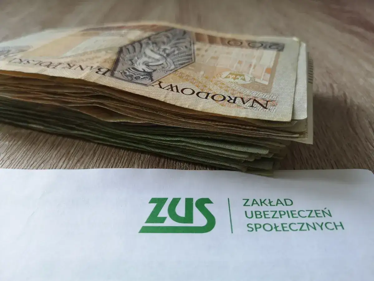 Stos banknot&oacute;w i logo ZUS. Gwarantowana wypłata z ZUS to pewność finansowa.