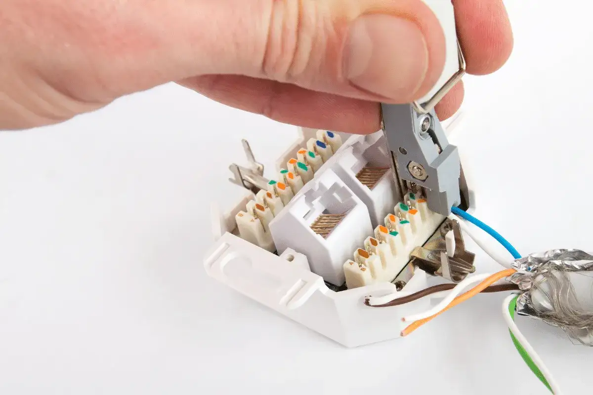 Hand legt Kabel mit Werkzeug auf Netzwerkdose auf.