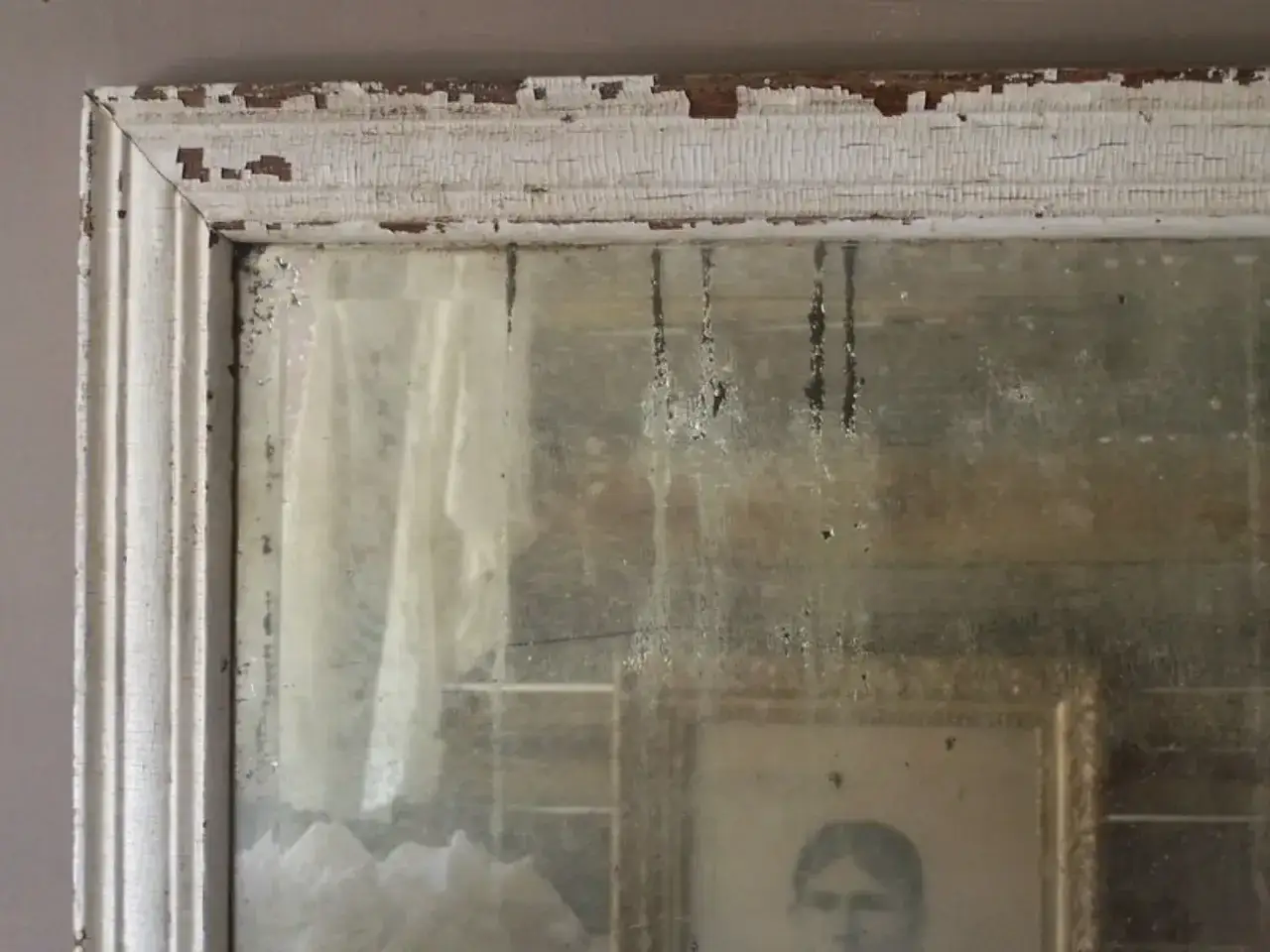 Dettagli di un vecchio specchio con cornice bianca scrostata, che riflette un ritratto e un drappo. Un esempio di come invecchiare uno specchio per un effetto vintage.