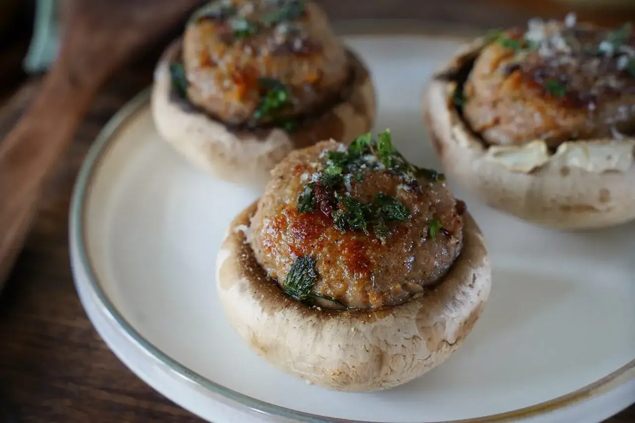 Trois champignons farcis, garnis d'une pr&eacute;paration savoureuse et parsem&eacute;s d'herbes fra&icirc;ches, reposent sur une assiette blanche.