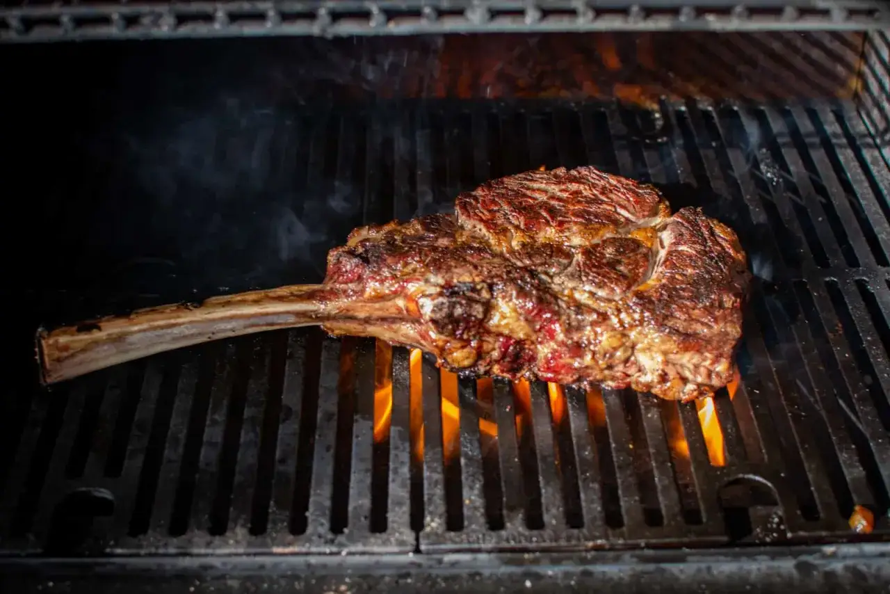 En saftig tomahawk-biff grillas &ouml;ver &ouml;ppna l&aring;gor. R&ouml;ken stiger och k&ouml;ttet f&aring;r en perfekt yta.