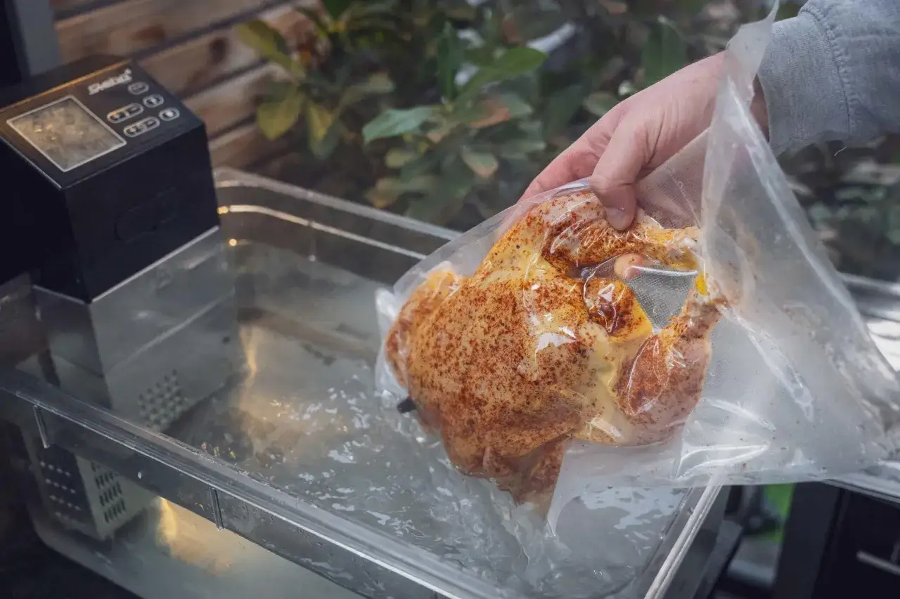 Ein ganzes Hähnchen, gewürzt und vakuumiert, wird in ein Wasserbad zum sous vide garen abgesenkt.