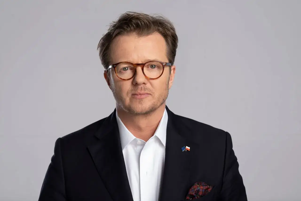 Michał Wawrykiewicz, prawnik i aktywista, w garniturze z flagami Polski i UE. Jego życiorys to historia walki o prawa obywatelskie.
