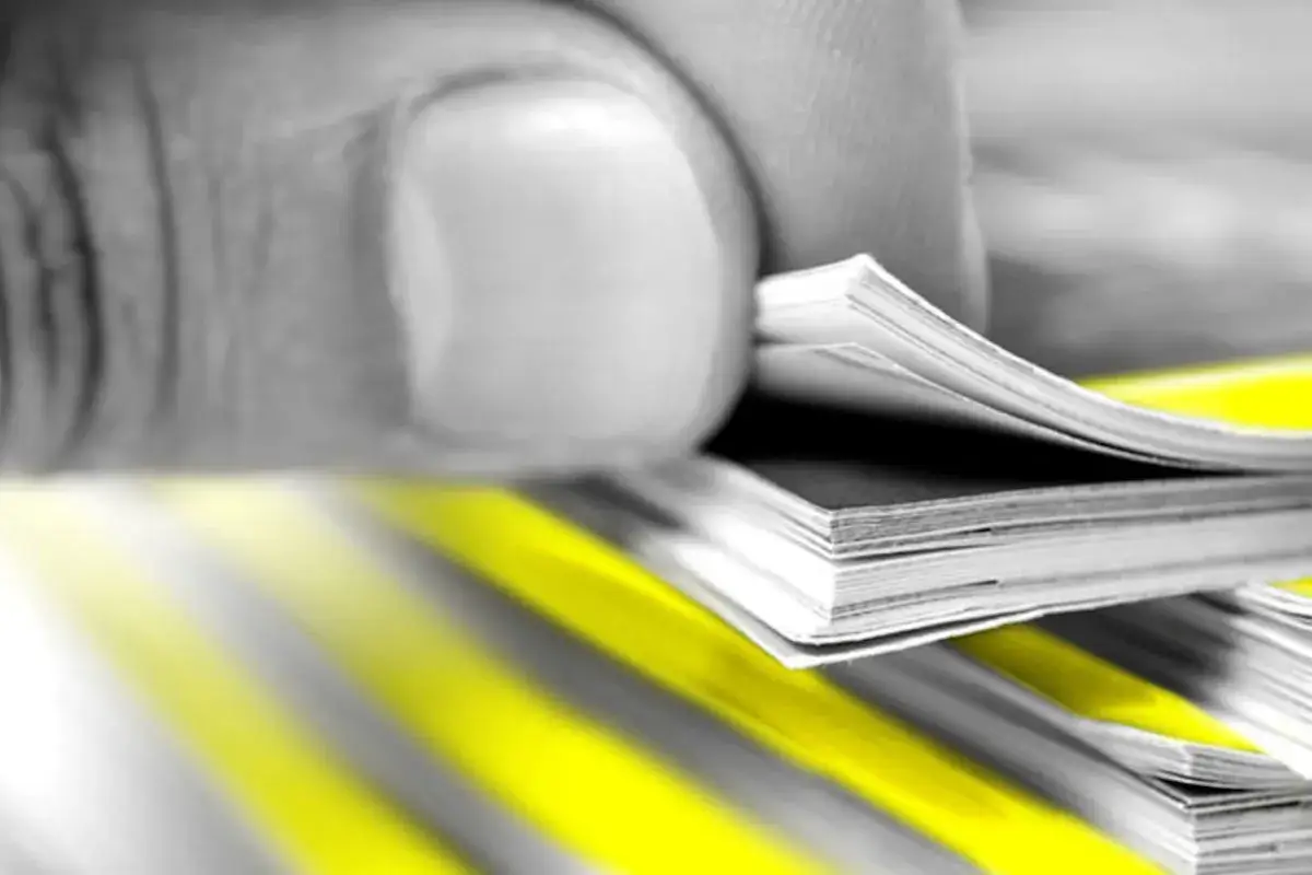 Dedo hojeando un libro, mostrando la densidad del papel y las vibrantes rayas amarillas.