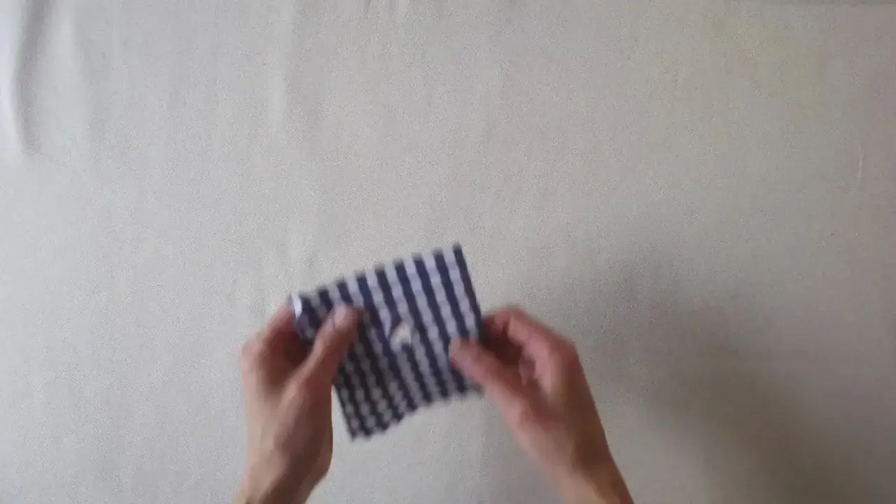Manos arreglan una ropa con un trozo de tela a cuadros azul y blanco, mostrando c&oacute;mo reparar una prenda.