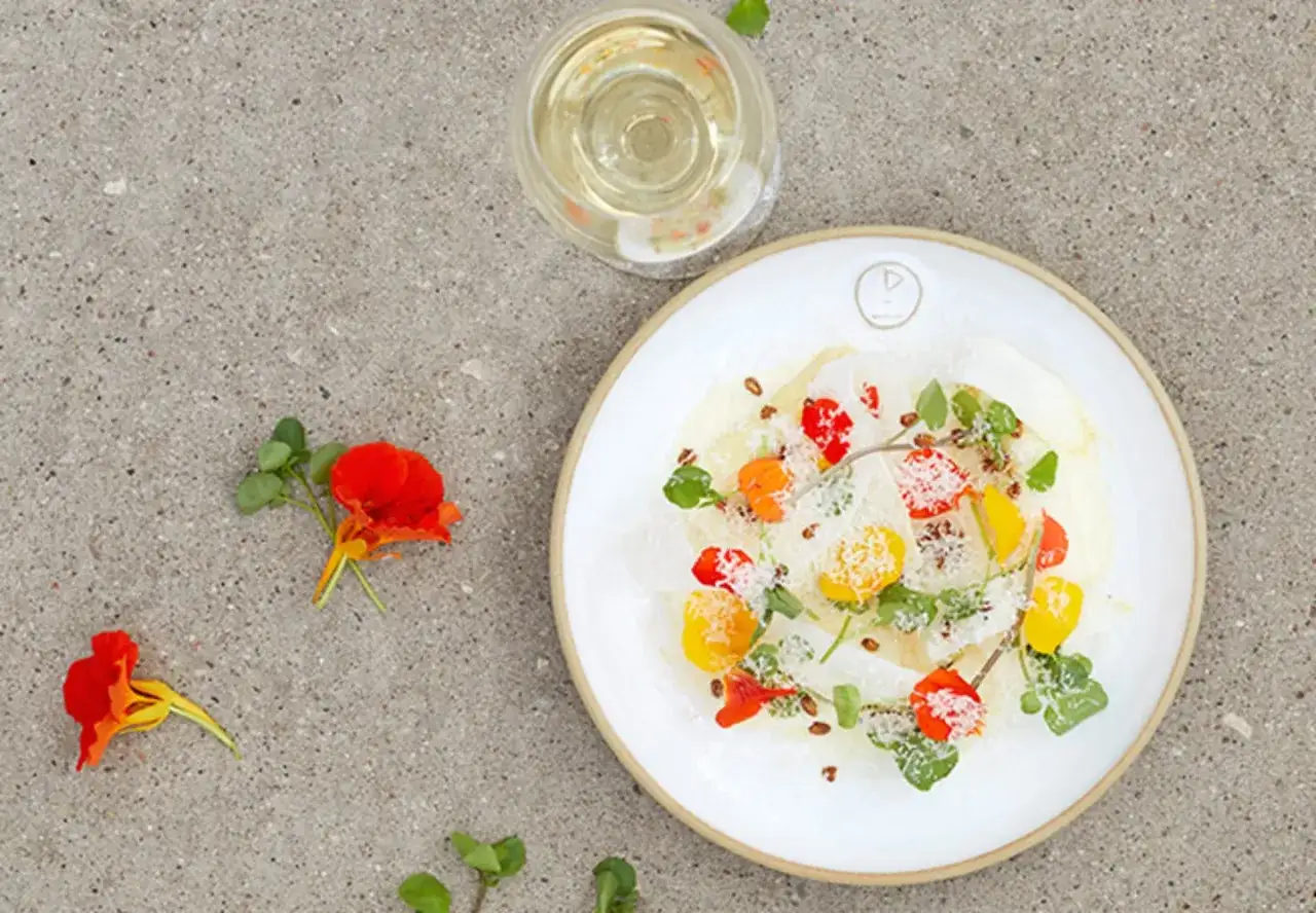 En vacker tallrik med vit sparris, garnerad med blommor och örter, bredvid ett glas vitt vin.