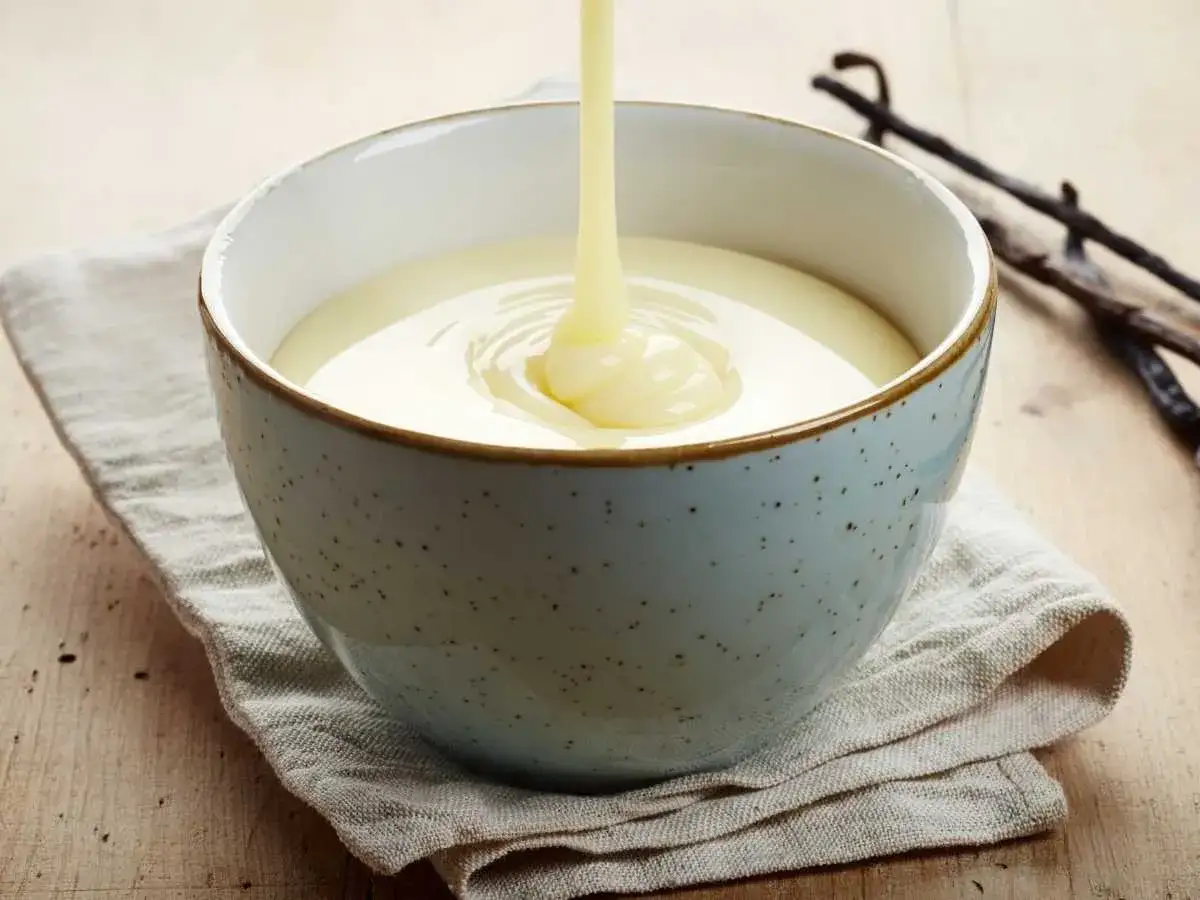 Crema inglesa verti&eacute;ndose en un cuenco azul, con vainas de vainilla al fondo.