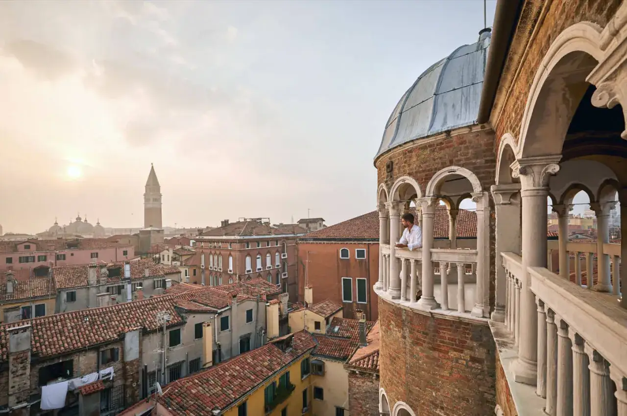 Uomo su balcone con vista sui tetti di Venezia. La **scala chiocciola Venezia** porta a questo panorama mozzafiato.