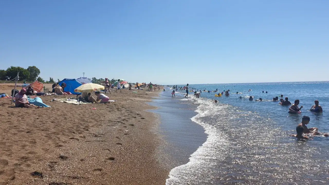 Słoneczna plaża w Lara, Turcja. Ludzie odpoczywają pod parasolami i kąpią się w morzu.