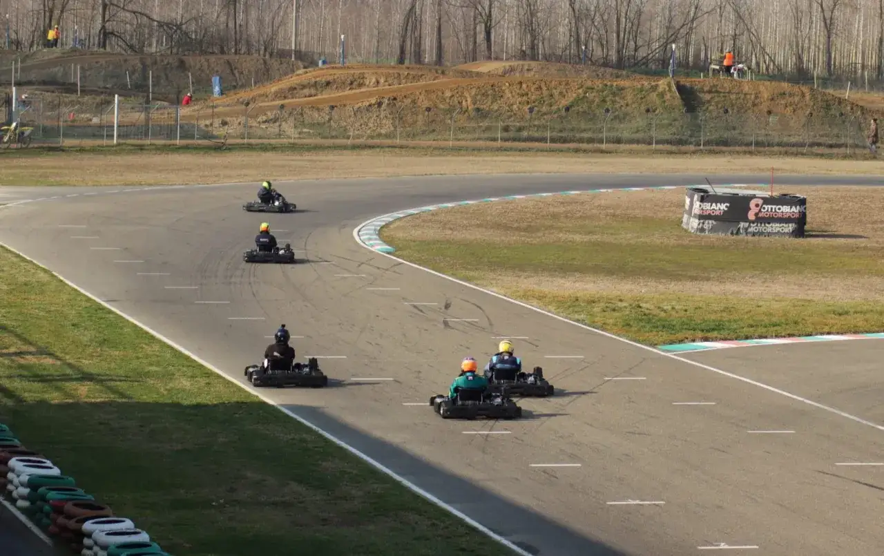 Gara di go-kart su pista con cartelloni Ottobiano Motorsport. Piloti in azione, sullo sfondo colline e alberi spogli.