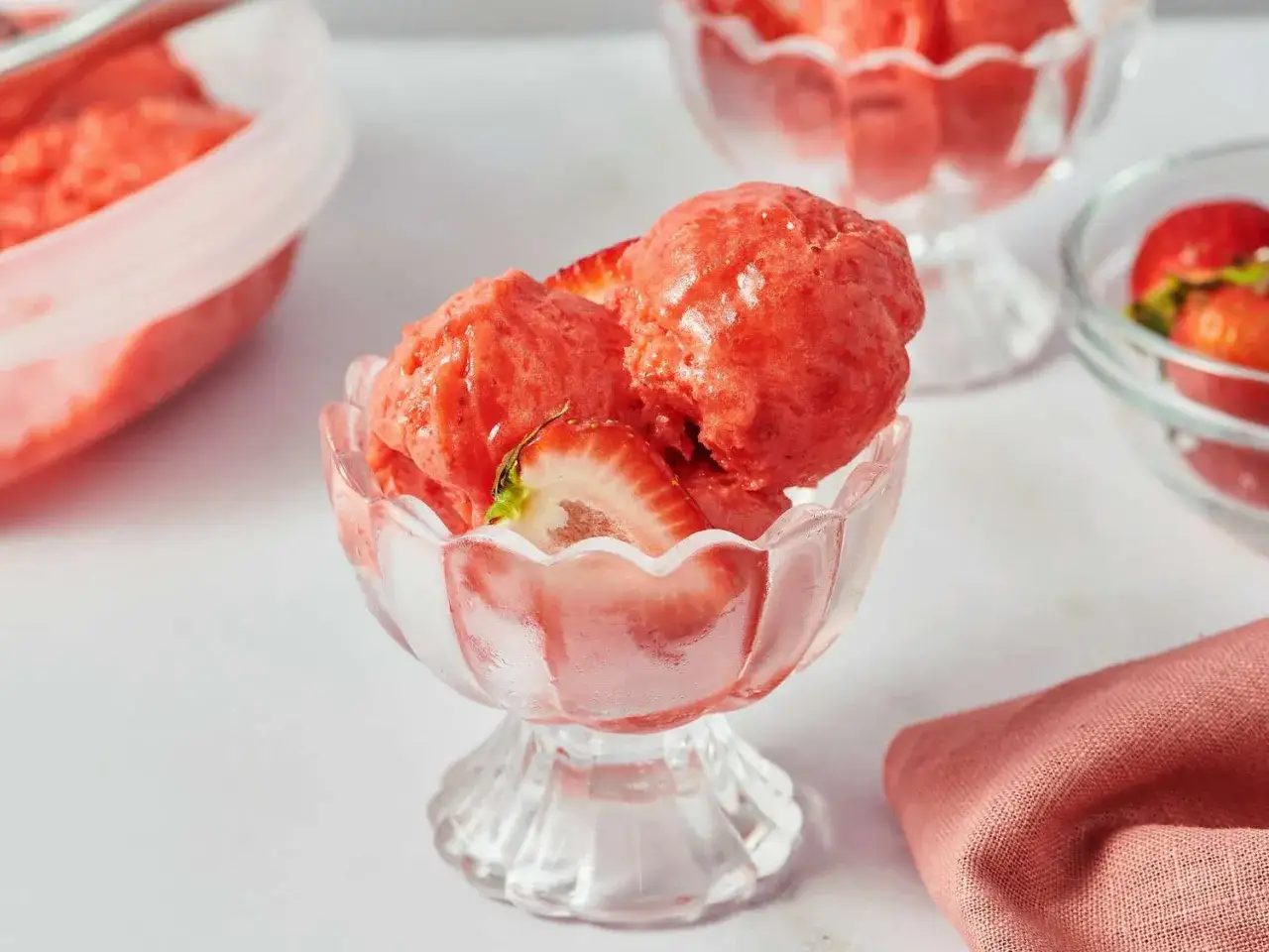 Trois boules de sorbet fraise dans un joli bol en verre, garnies de fraises fra&icirc;ches. Un d&eacute;lice rafra&icirc;chissant.