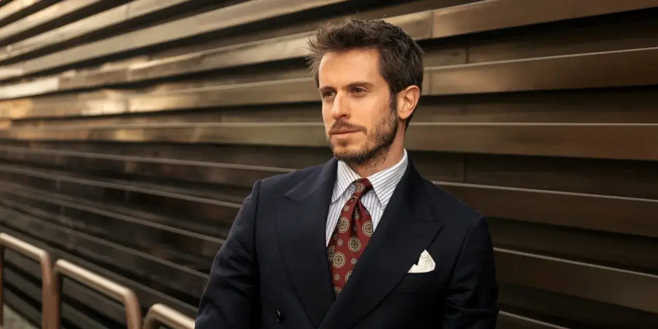 Uomo con abito nero, camicia a righe e cravatta blu con fantasia. Sguardo pensieroso.