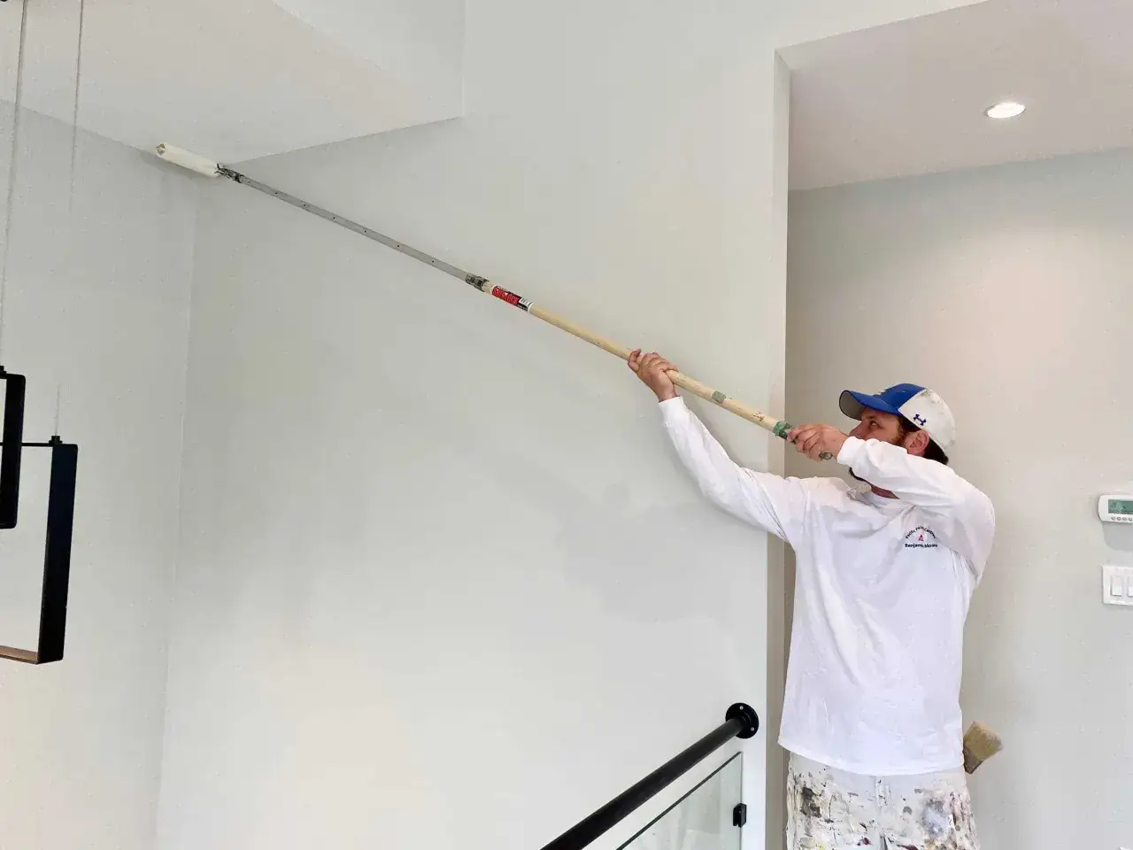 Un peintre utilise un rouleau à long manche pour peindre un plafond blanc. Un schéma pour peindre un plafond est en cours de réalisation.