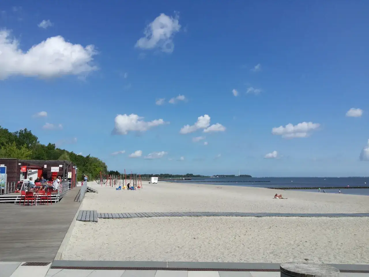 Ein sonniger Tag am **Stralsund Strand**. Menschen entspannen sich im Sand, w&auml;hrend Kinder auf dem Spielplatz toben.